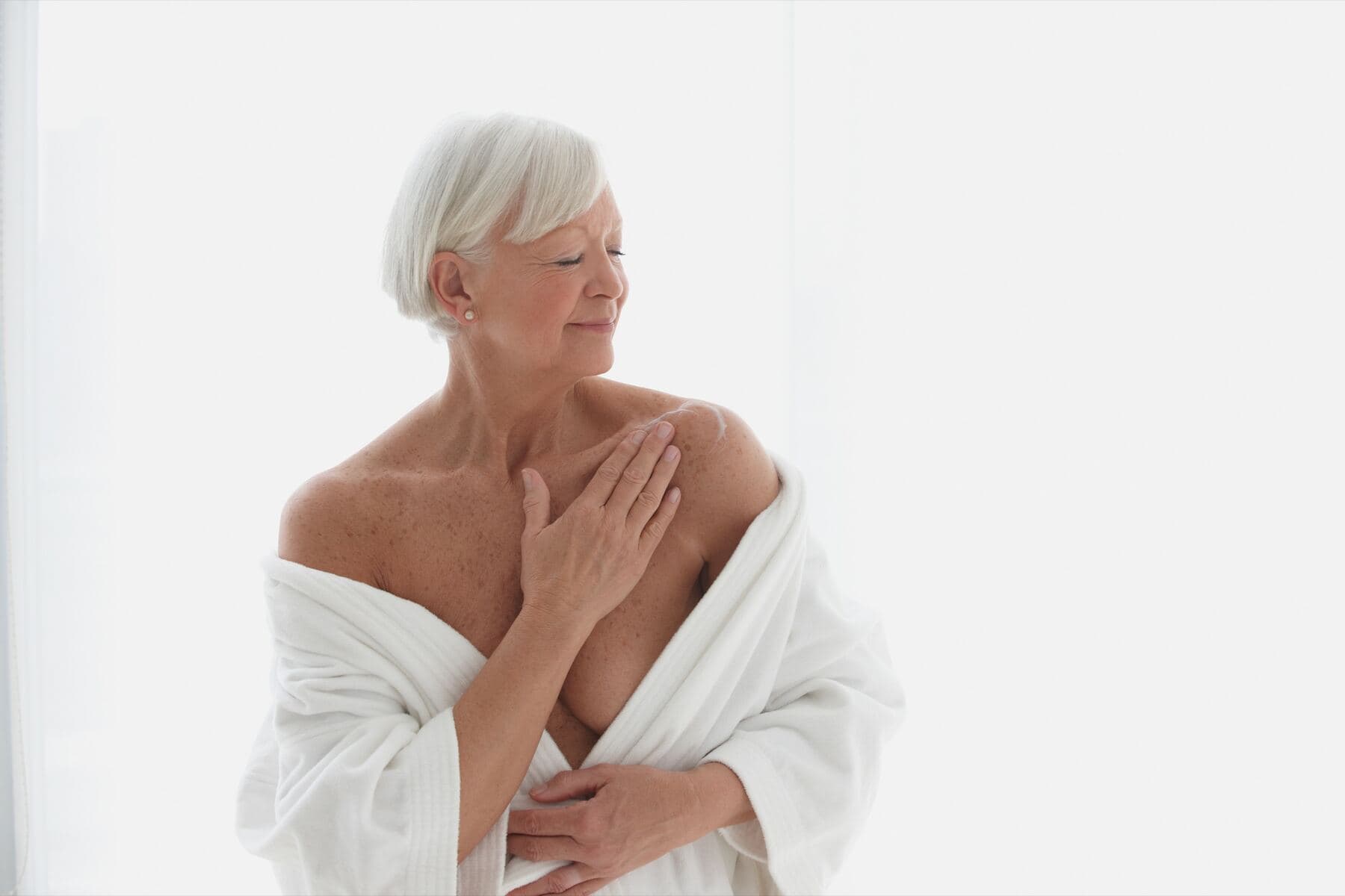 Femme aux cheveux blancs appliquant une lotion sur ses épaules