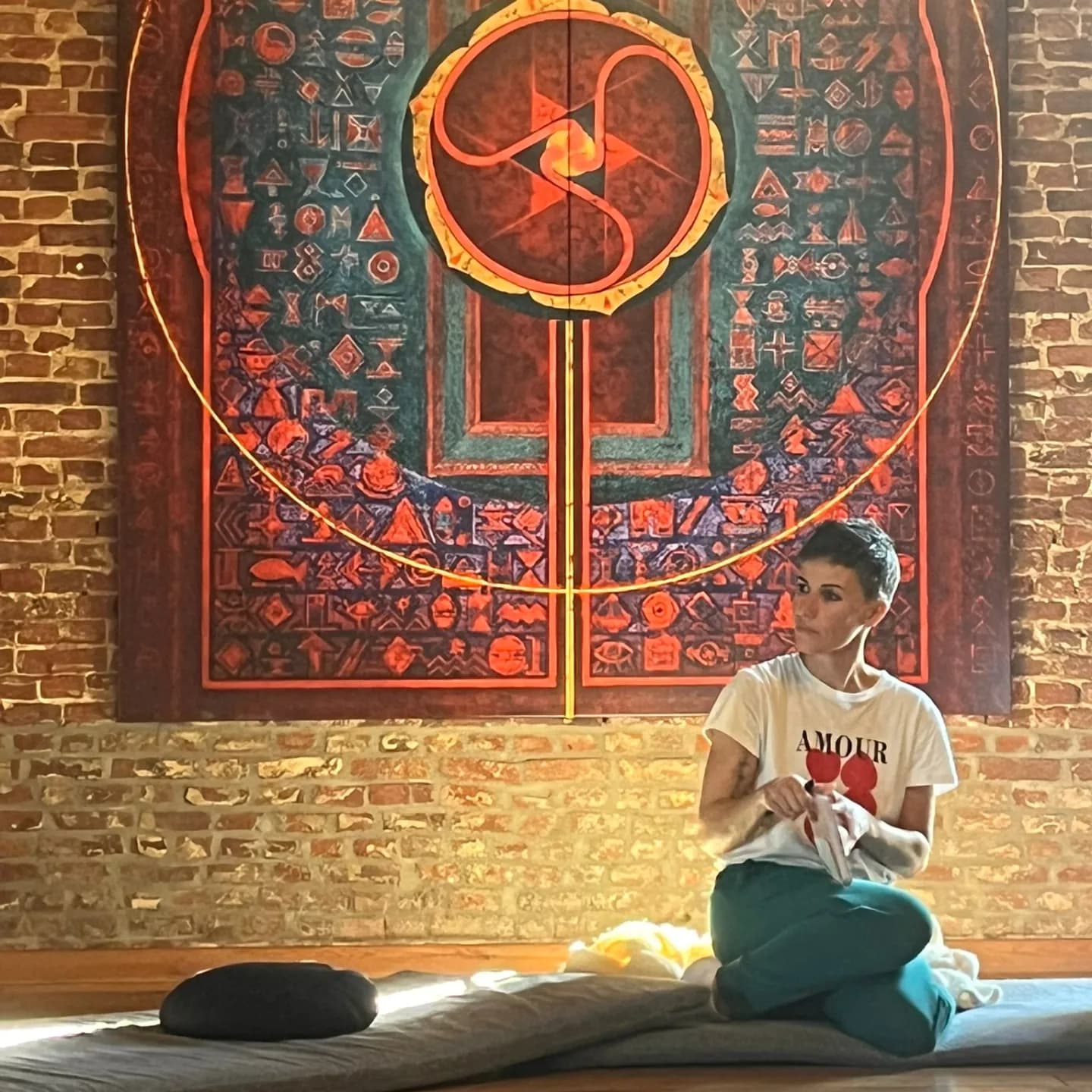 Delphine assise sur un futon dans l'espace de soin, devant une porte peinte d'un mandala